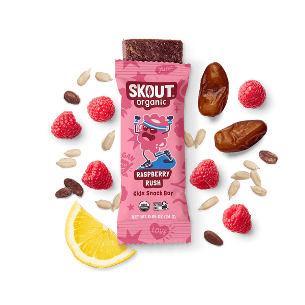 Skout Organic Raspberry Rush Kids Snack Bar in an open wrapper, surrounded by dates, raspberries, and a lemon wedge.